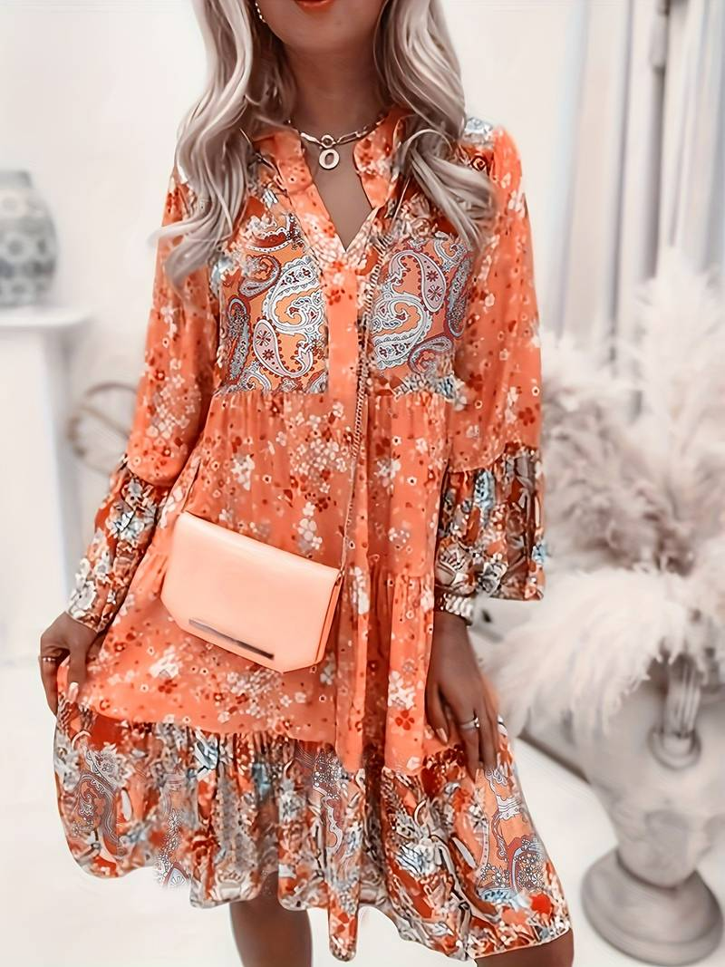 Woman wearing a floral dress with long sleeves and a pink handbag, standing indoors.