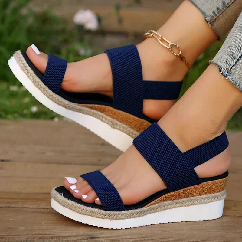Navy wedge sandals with jute sole worn by a person on a wooden surface.