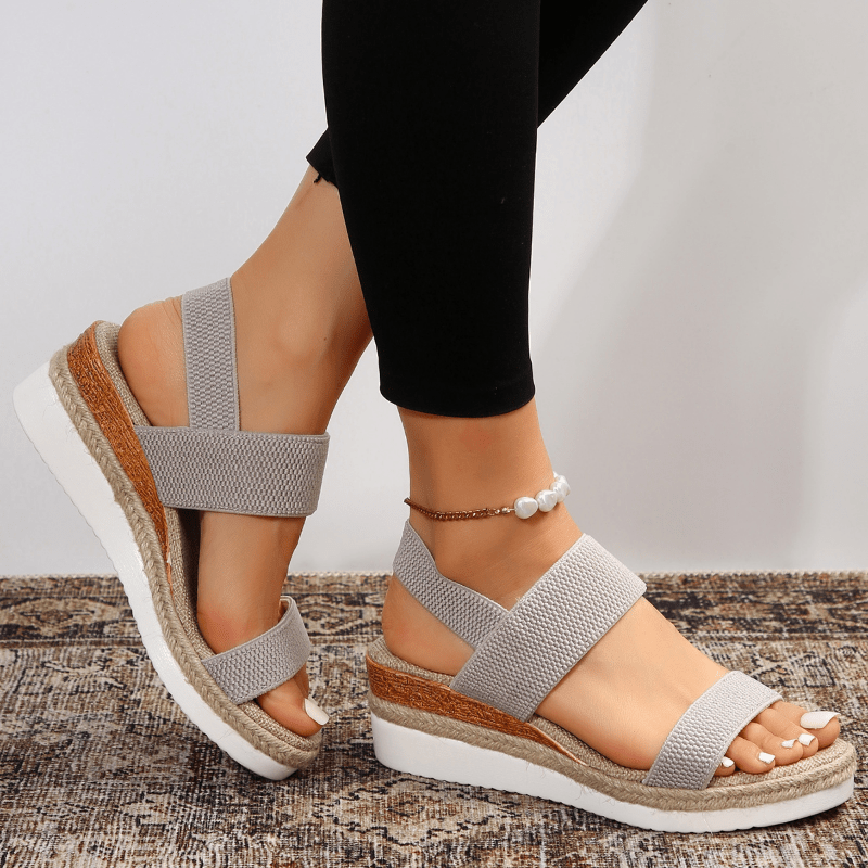 Gray sandals with jute sole worn by a person on a textured surface.