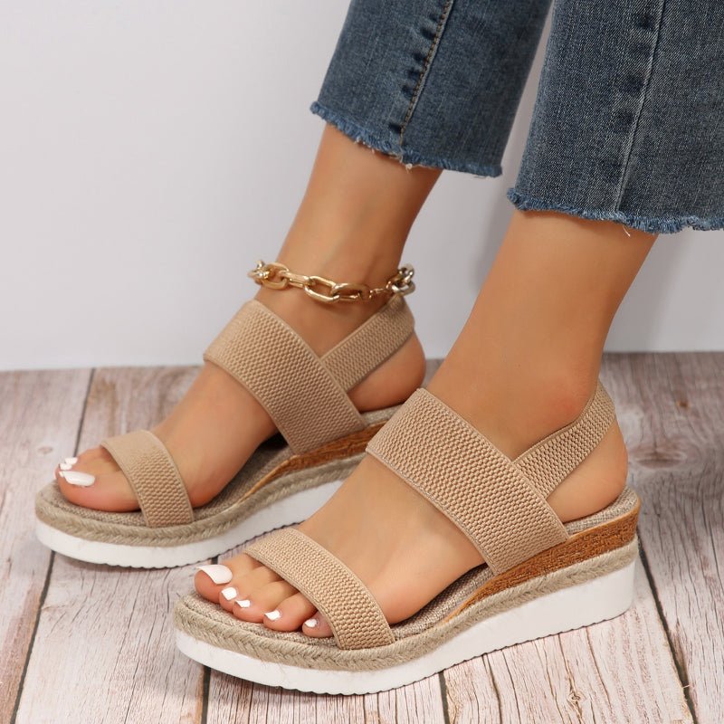 Beige sandals with white soles worn by a person on a wooden floor.