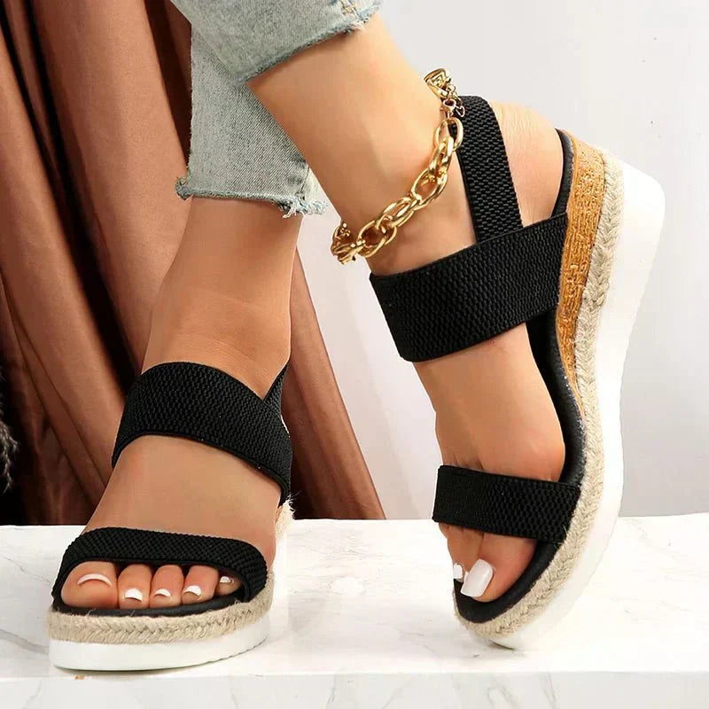 Black wedge sandals with cork sole worn by a person on a white background