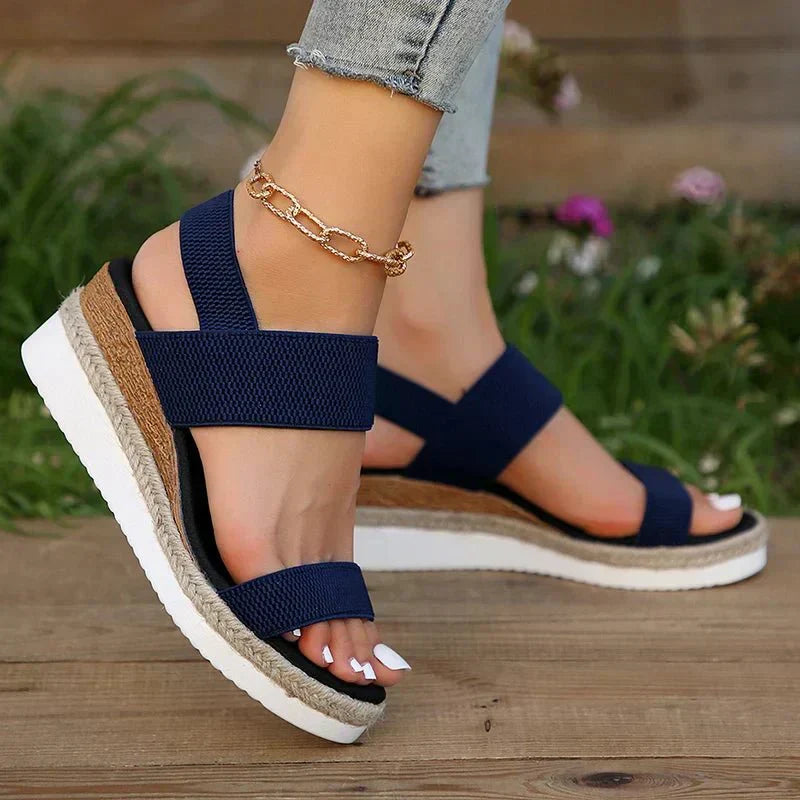 Navy sandals with a braided sole worn on a wooden surface with a blurred natural background