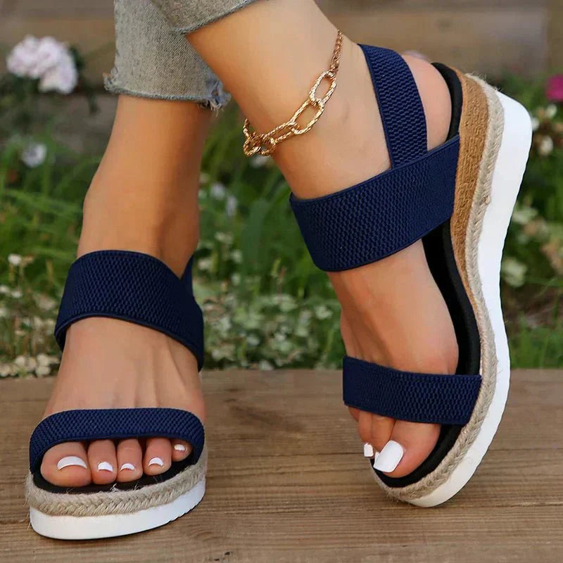 Navy blue sandals with white soles worn by a person on a wooden surface with a blurred floral background.
