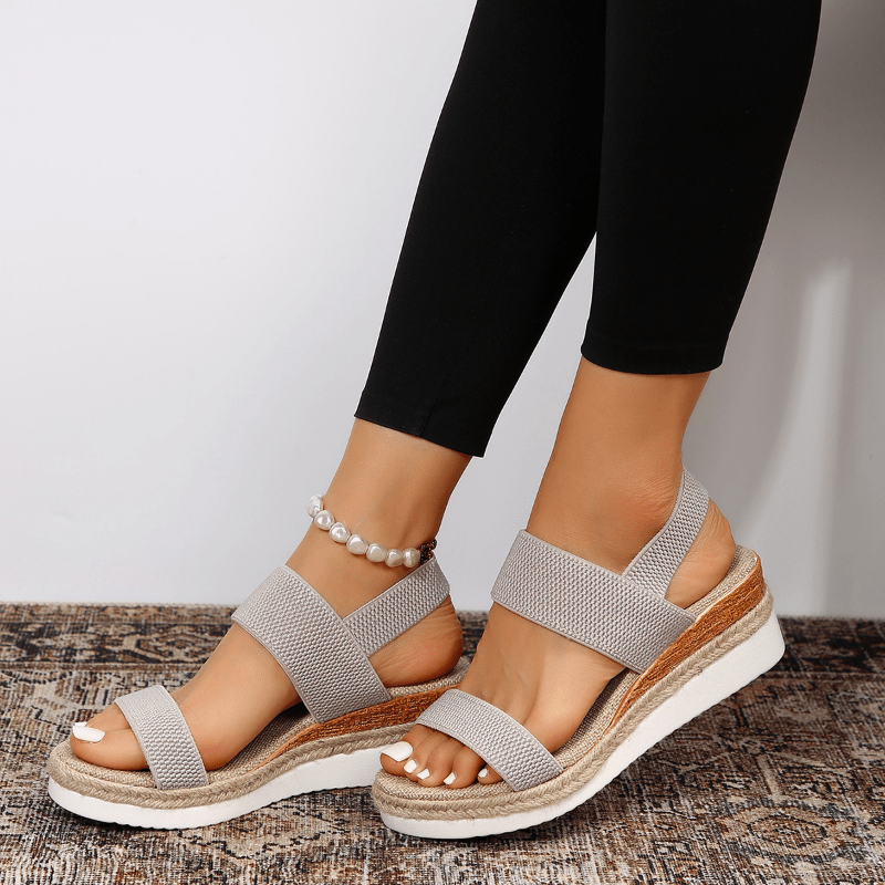 Gray sandals worn with black leggings on a neutral background