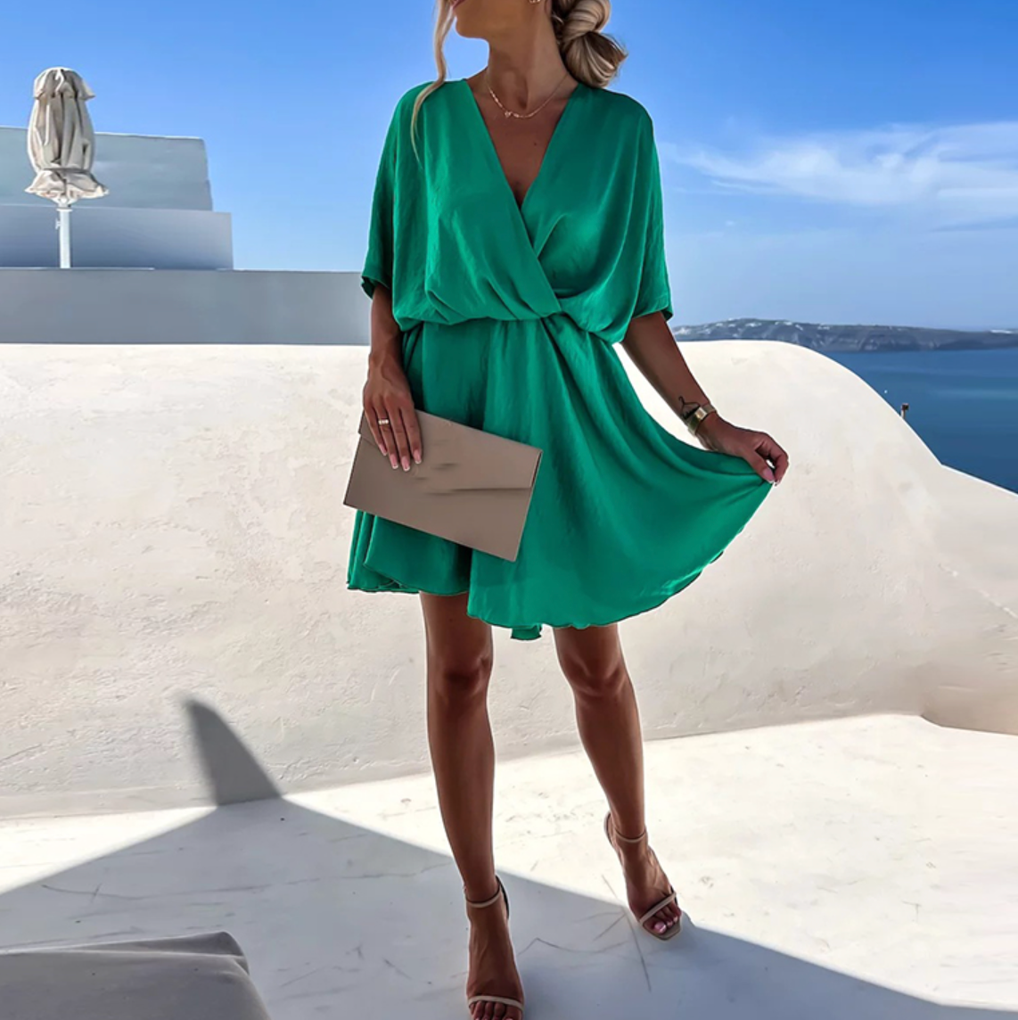 Woman in a green dress standing on a white ledge with a blue sky and ocean background