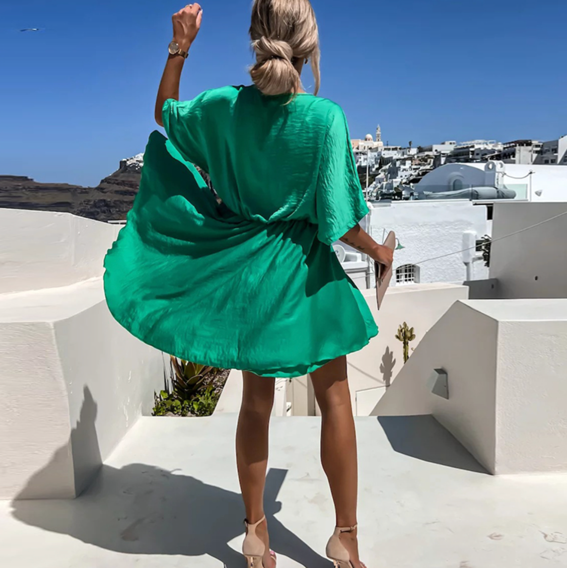Woman in a green dress standing on a white rooftop with a scenic view of white buildings and blue sky.