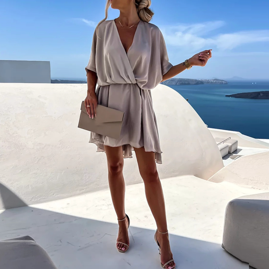 Woman in a beige dress standing on a rooftop with a scenic ocean view.