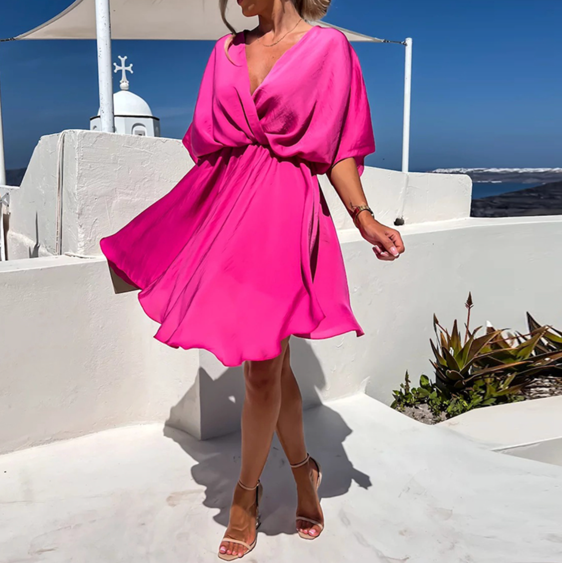 Woman in a bright pink dress standing on a white ledge with ocean view