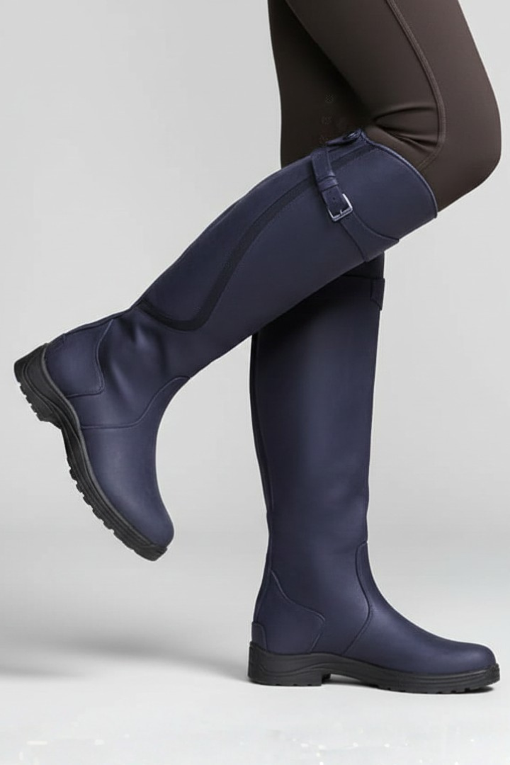 Navy riding boots worn with black pants on a light gray background