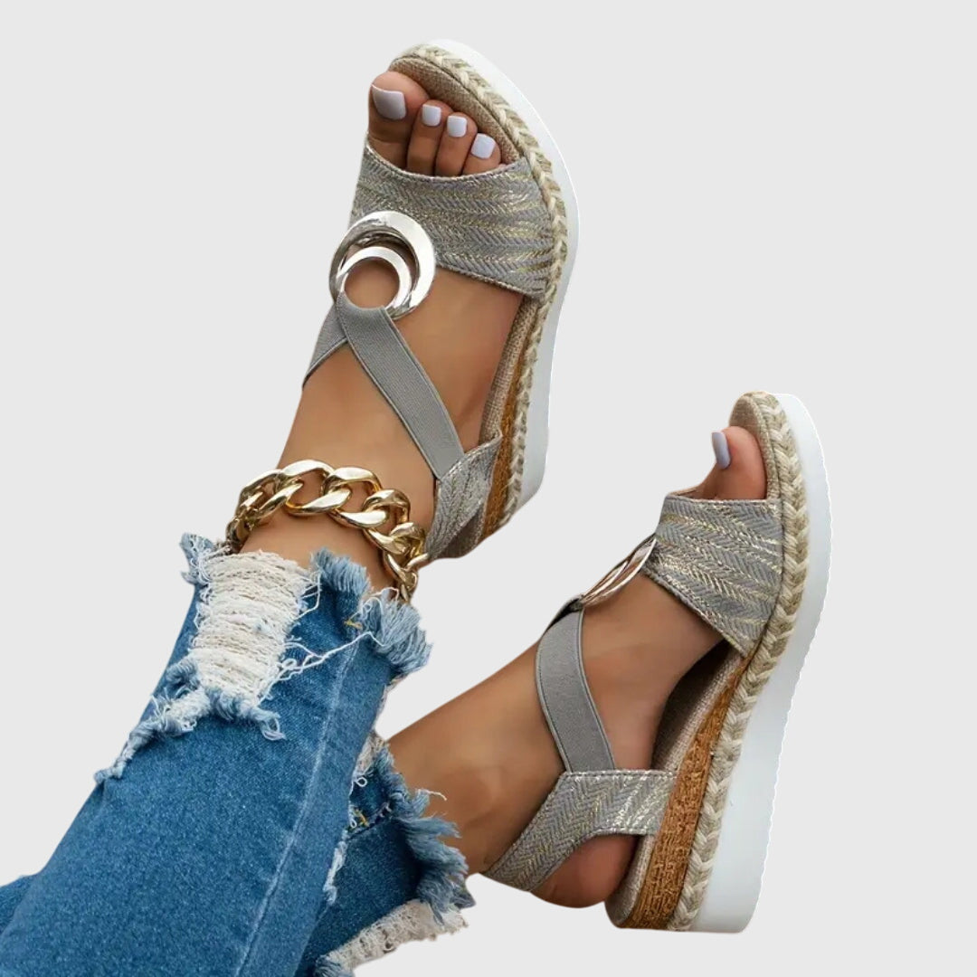 Silver wedge sandals with gold chain detail worn with ripped jeans on a light gray background