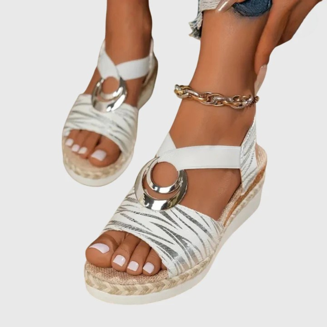 White wedge sandals with metallic accents worn by a person on a light gray background