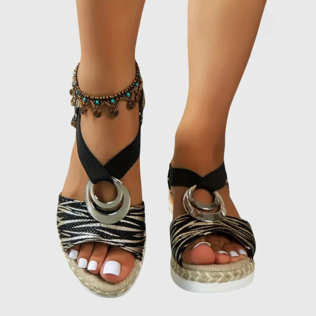 Black strappy sandals with circular metal details worn by a person on a light gray background