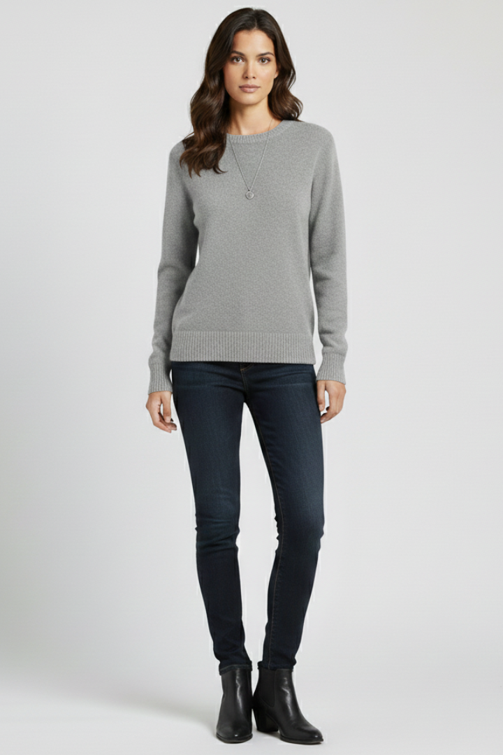 Woman wearing a gray sweater and dark jeans on a white background