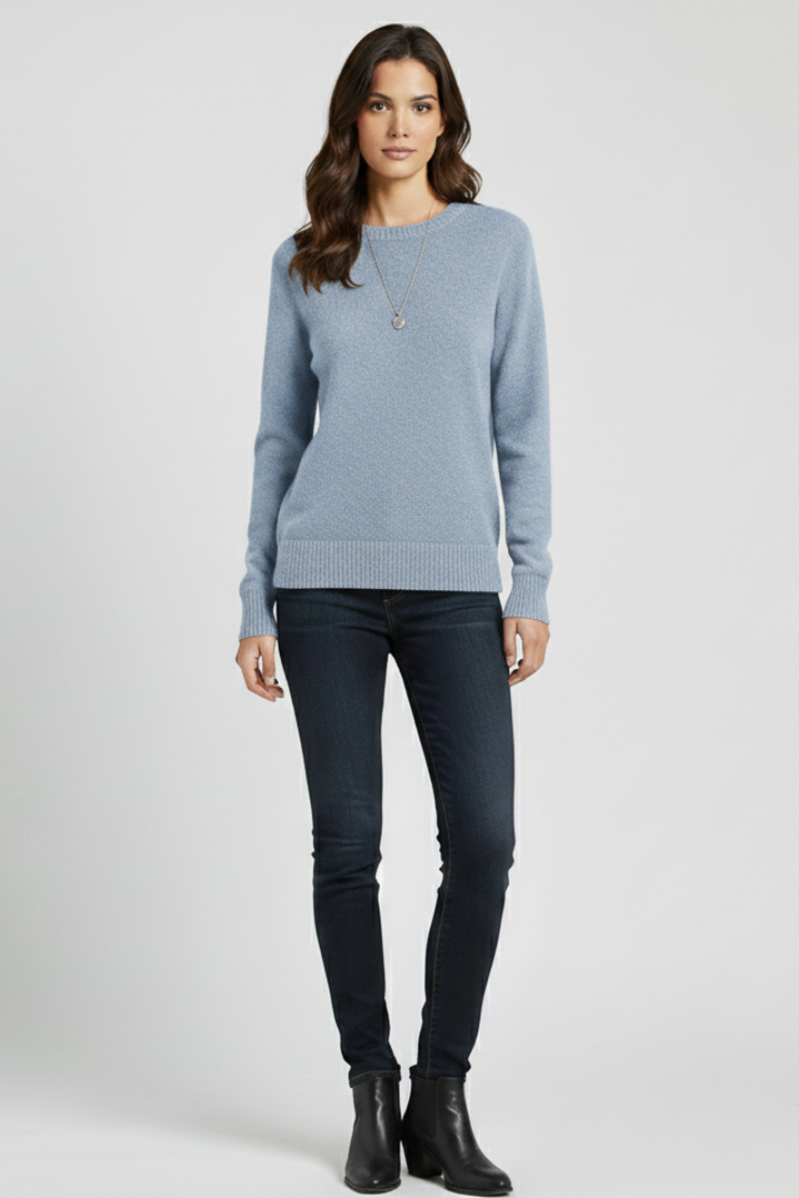 Woman wearing a light blue sweater and dark jeans on a white background
