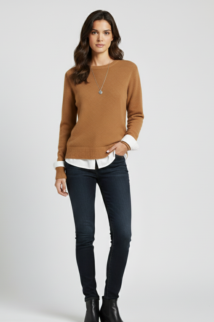 Woman wearing a brown sweater, white shirt, dark jeans, and black boots on a white background