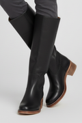 Black knee-high boots with brown soles worn by a person on a light gray background