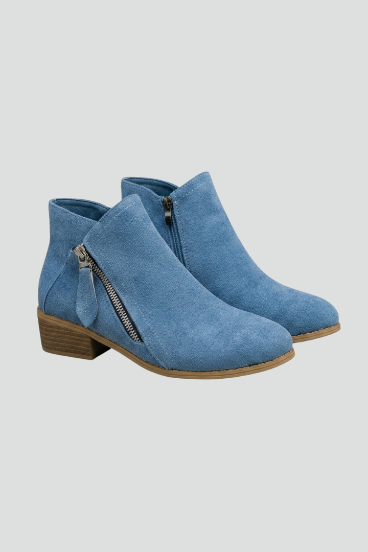 Pair of blue suede ankle boots with zippers on a light gray background