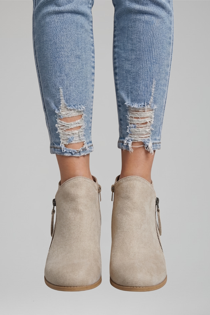 Beige ankle boots worn with distressed blue jeans on a gray background
