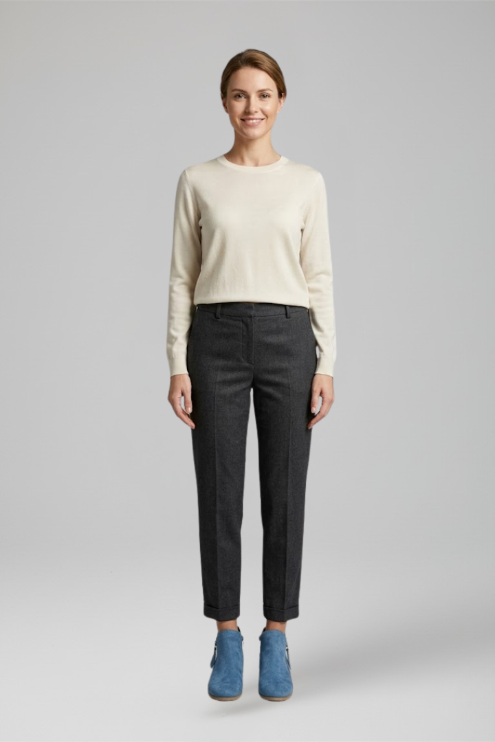Woman wearing a beige sweater and black pants on a gray background
