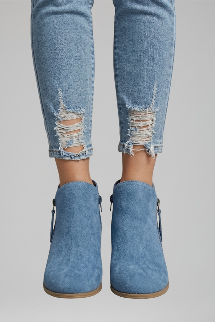 Blue denim ankle boots worn with distressed jeans on a gray background