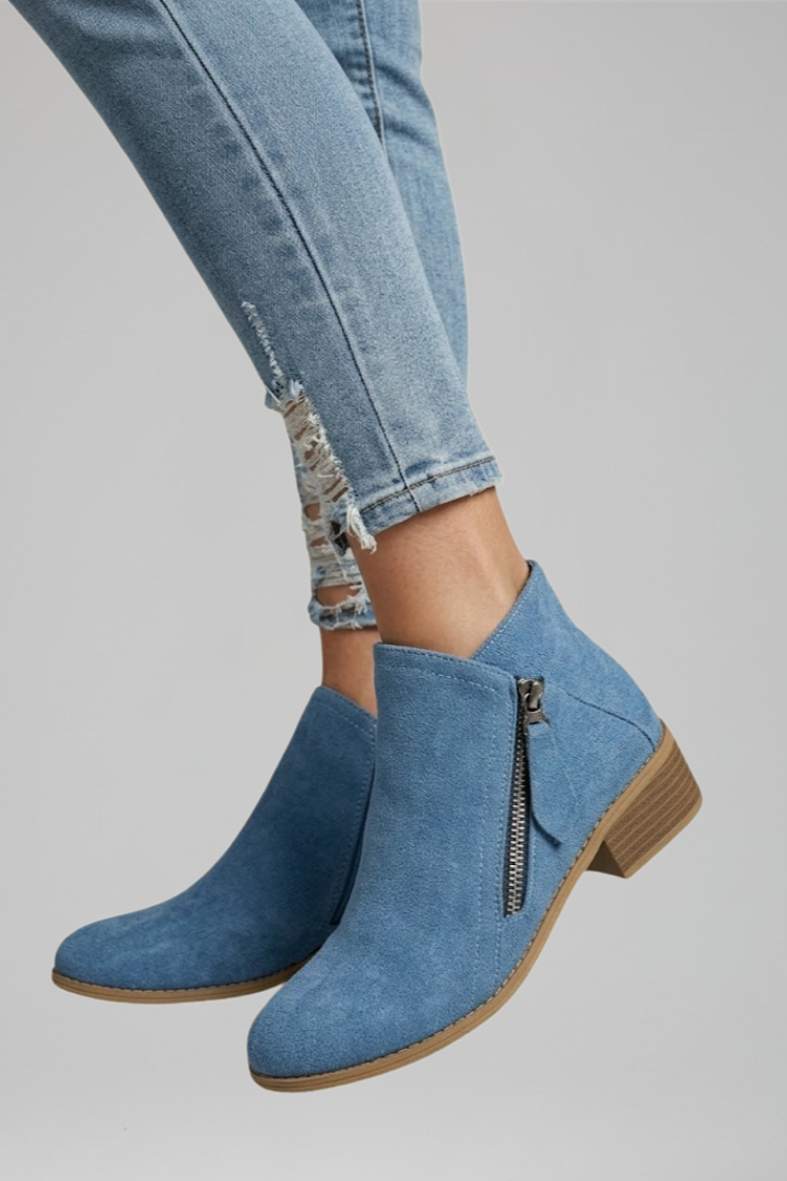 Blue denim ankle boots worn with light blue jeans on a gray background