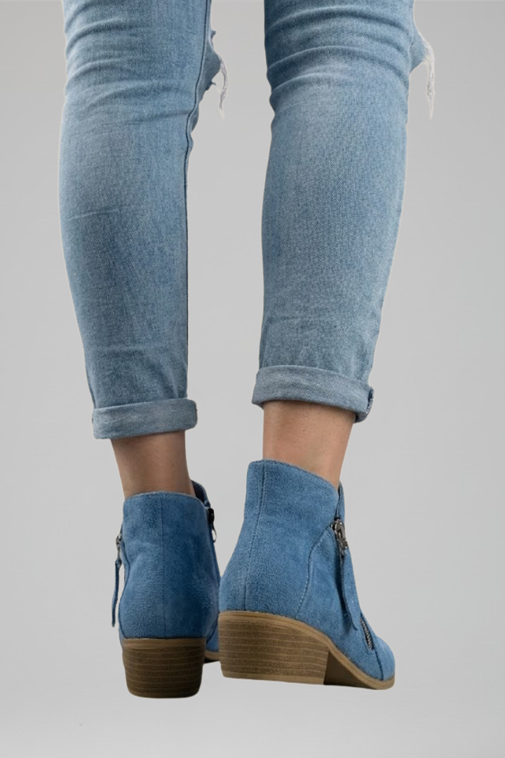 Blue denim ankle boots worn with light blue jeans on a gray background
