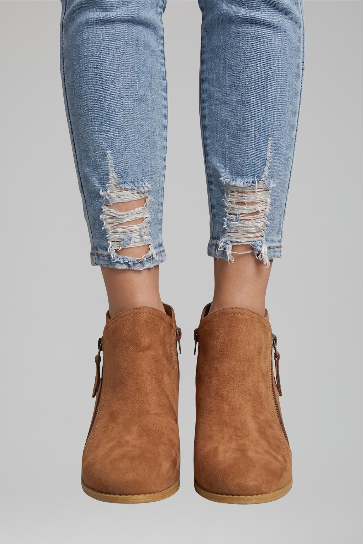Brown ankle boots worn with ripped blue jeans on a gray background