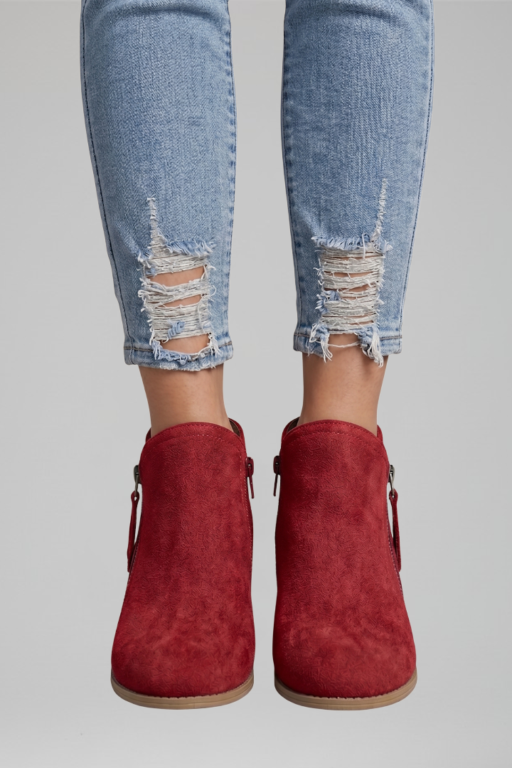 Red ankle boots worn with ripped jeans on a plain background
