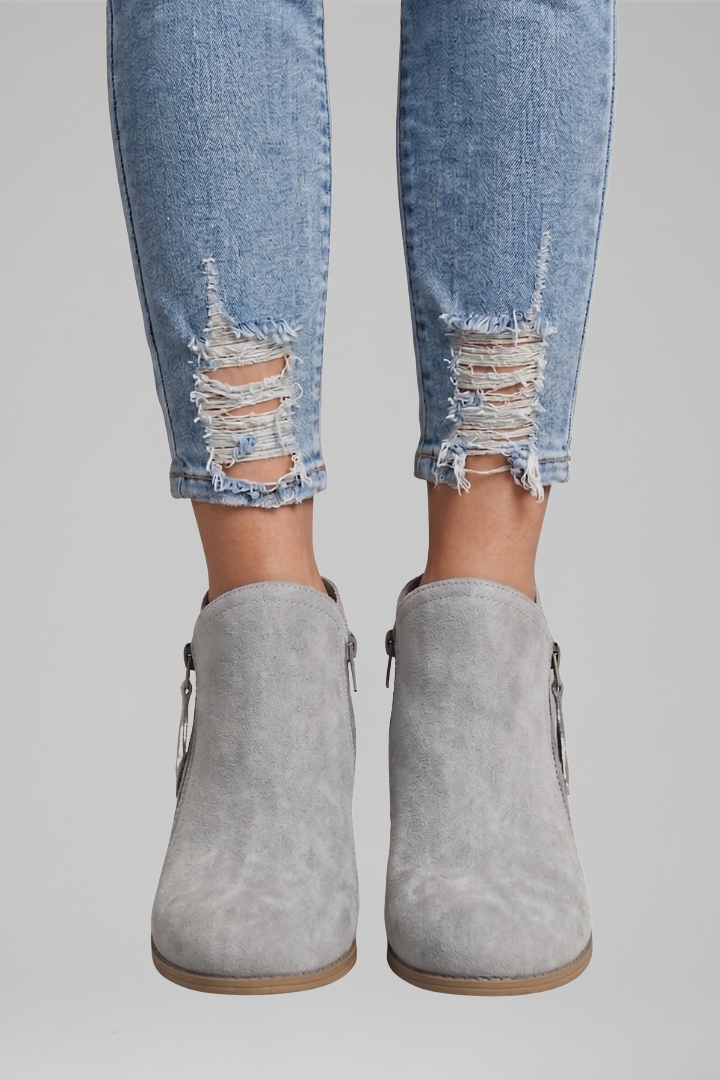Gray ankle boots worn with distressed blue jeans on a gray background