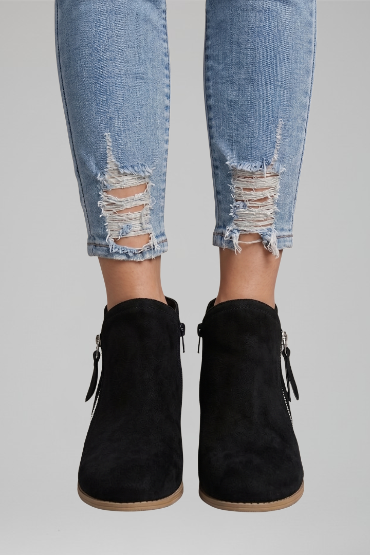 Black ankle boots worn with distressed jeans on a gray background