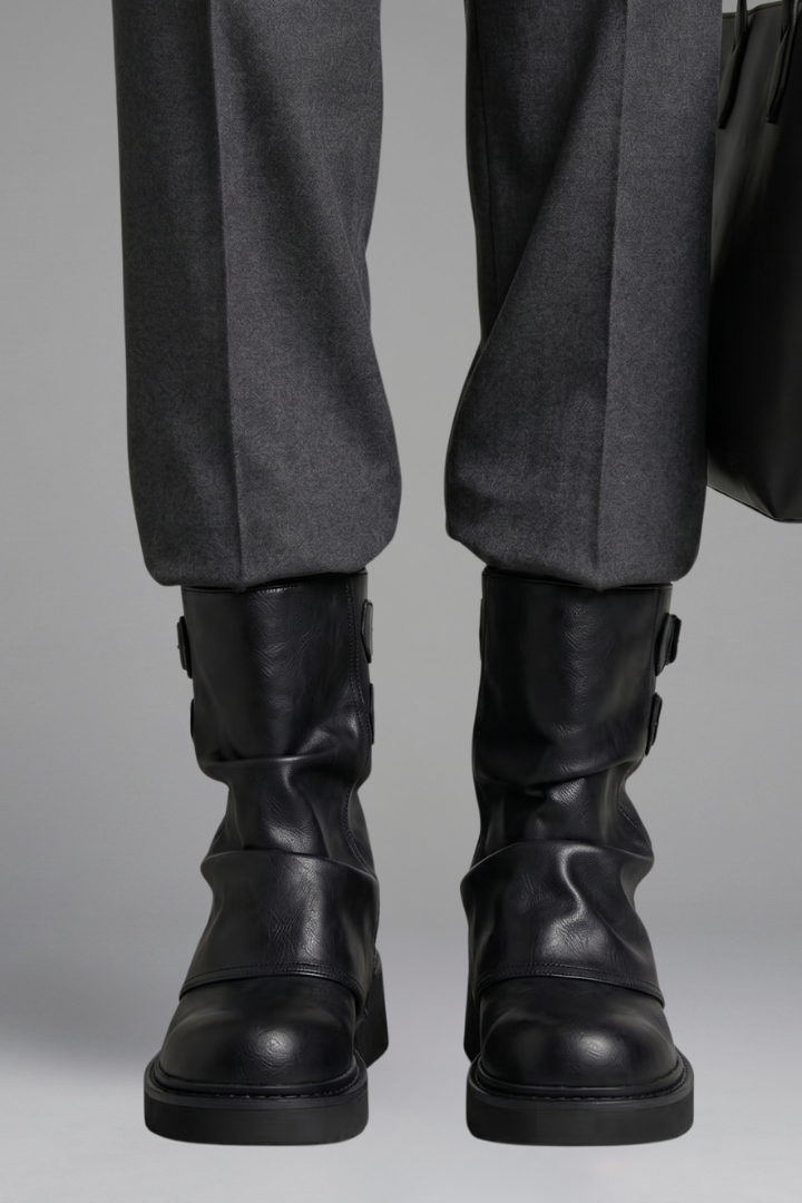 Black leather boots worn with gray pants on a neutral background