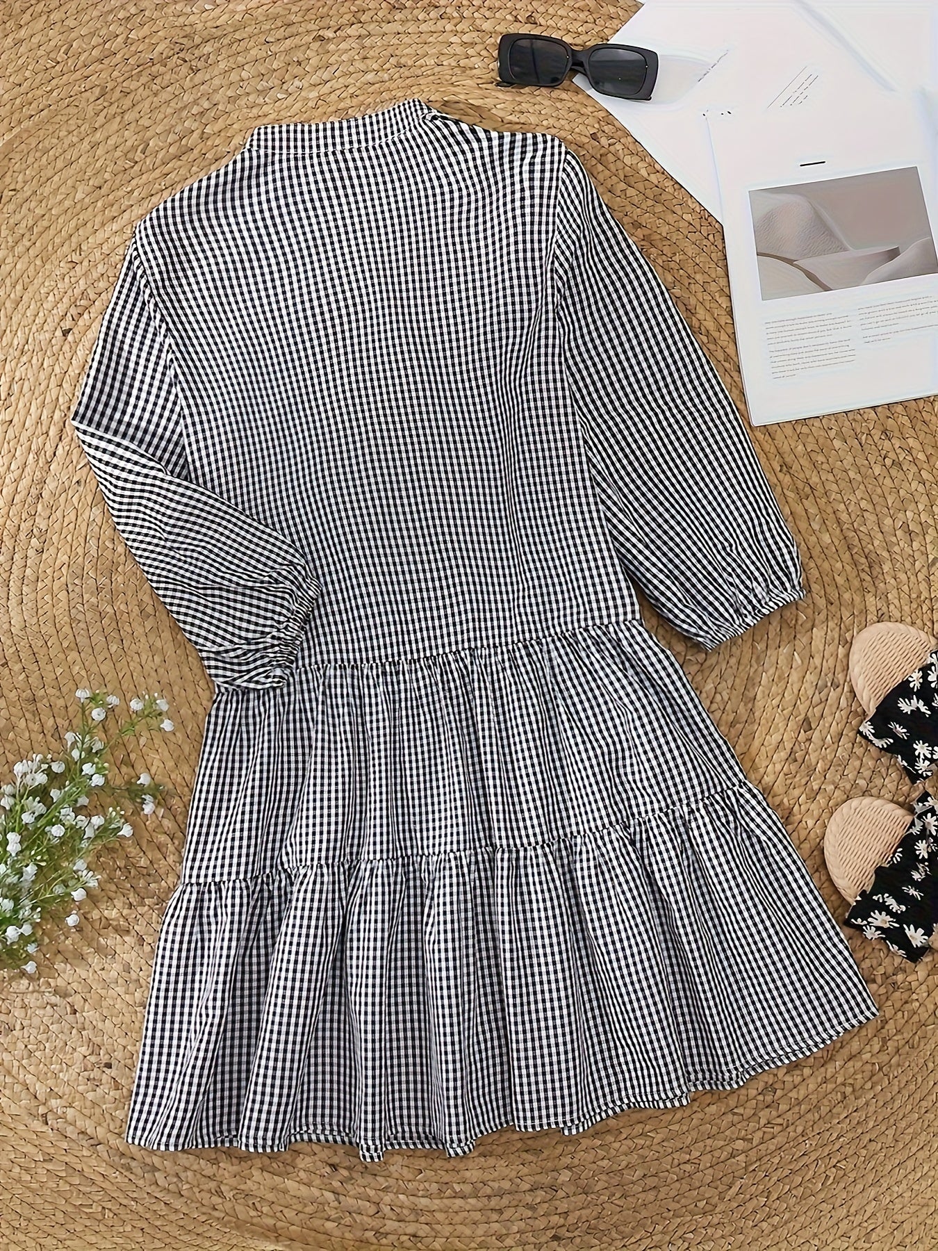 Black and white checkered dress on a textured surface with a bow and magazine in the background.