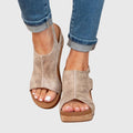 Beige open-toe wedges worn with rolled-up jeans on a light gray background