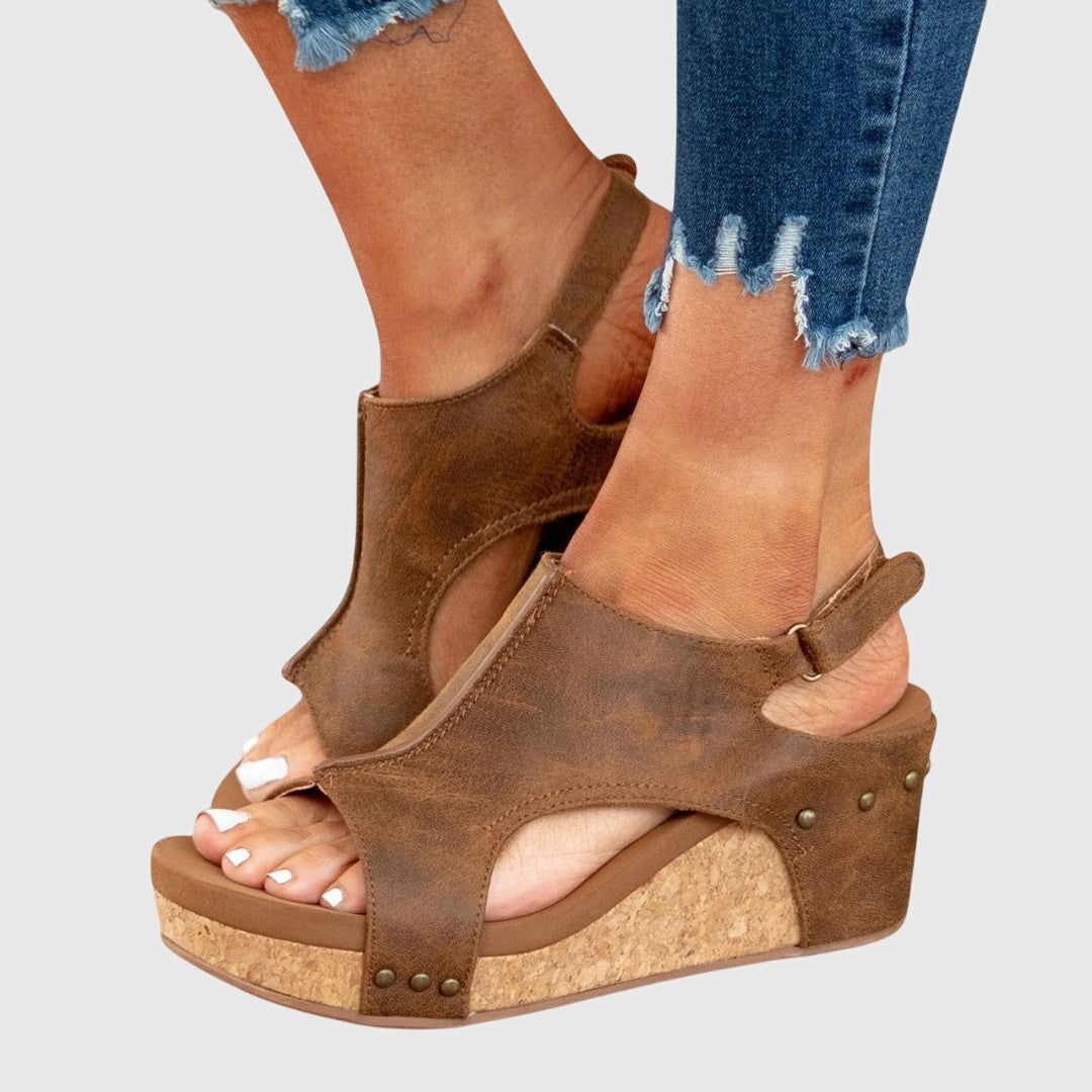 Brown wedge sandals worn with ripped jeans on a light gray background