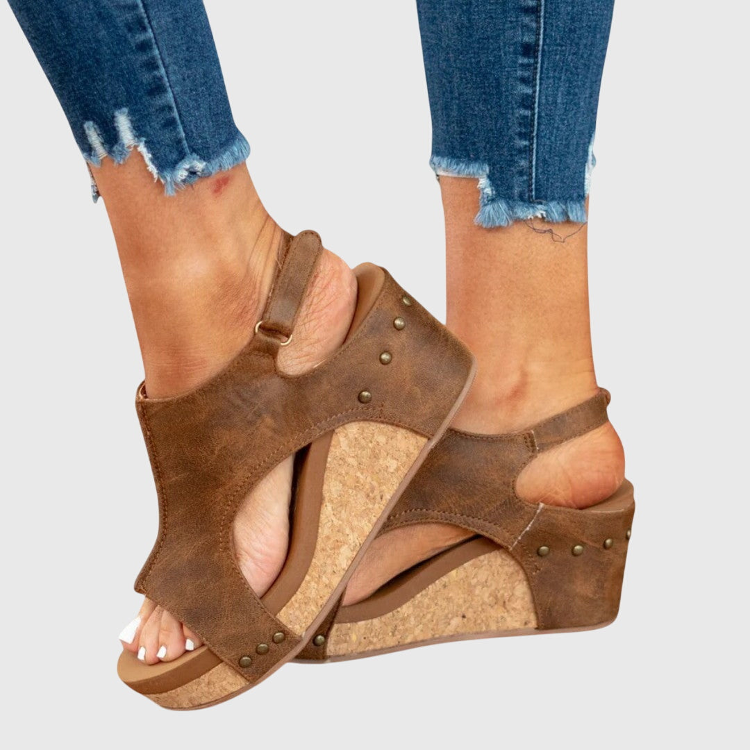 Brown wedge sandals worn with blue jeans on a light gray background