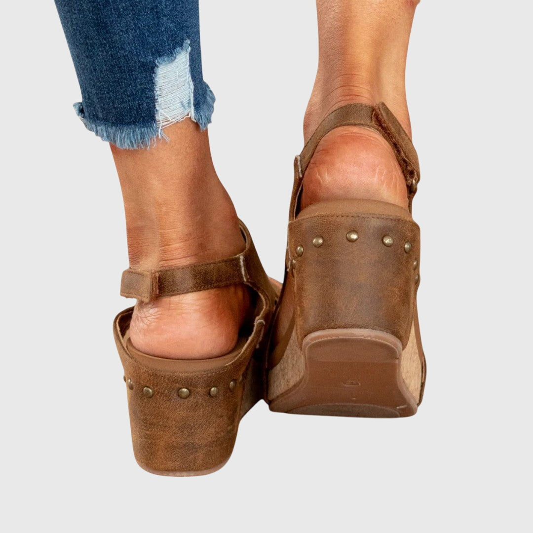 Brown platform sandals worn with ripped jeans on a light gray background