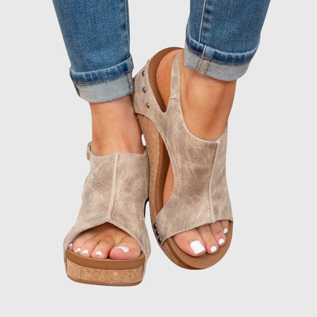 Beige wedge sandals worn with rolled-up jeans on a light gray background