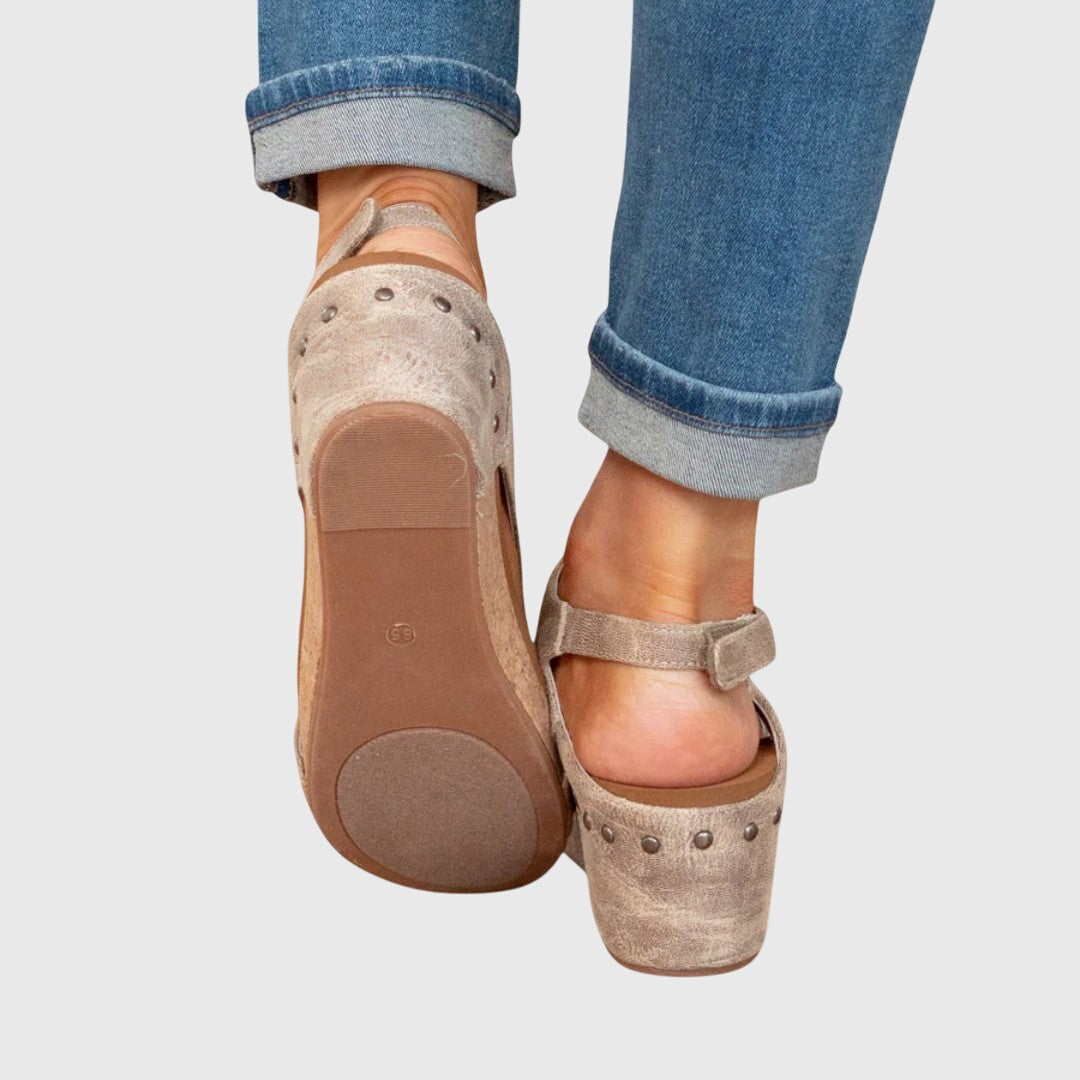 Beige wedge sandals worn with rolled-up blue jeans on a light gray background