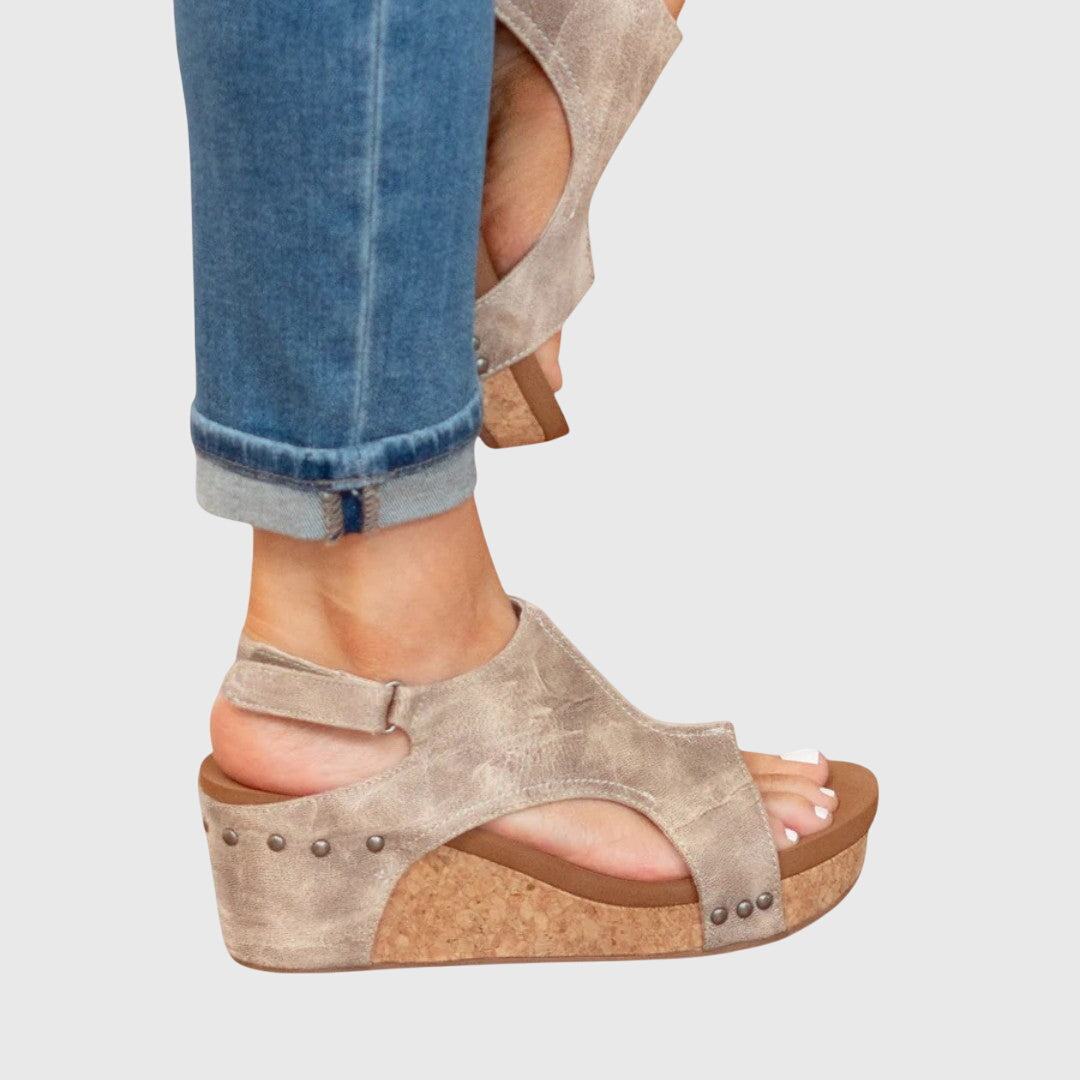 Beige wedge sandal worn with rolled-up jeans on a light gray background