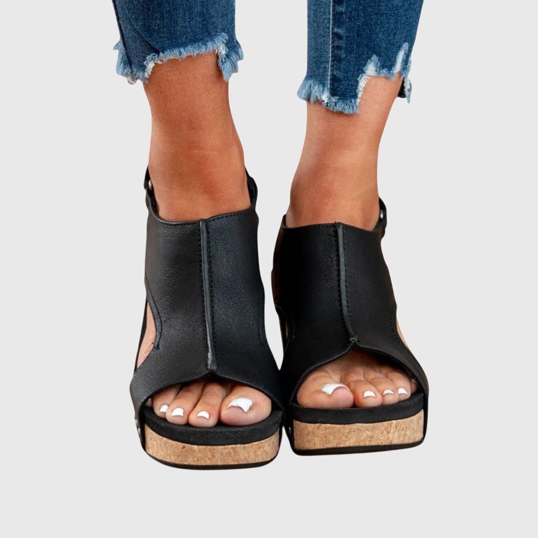 Black wedge sandals worn with rolled-up jeans on a light gray background