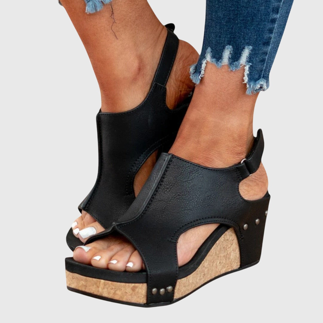 Black wedge sandals worn with ripped jeans on a light gray background
