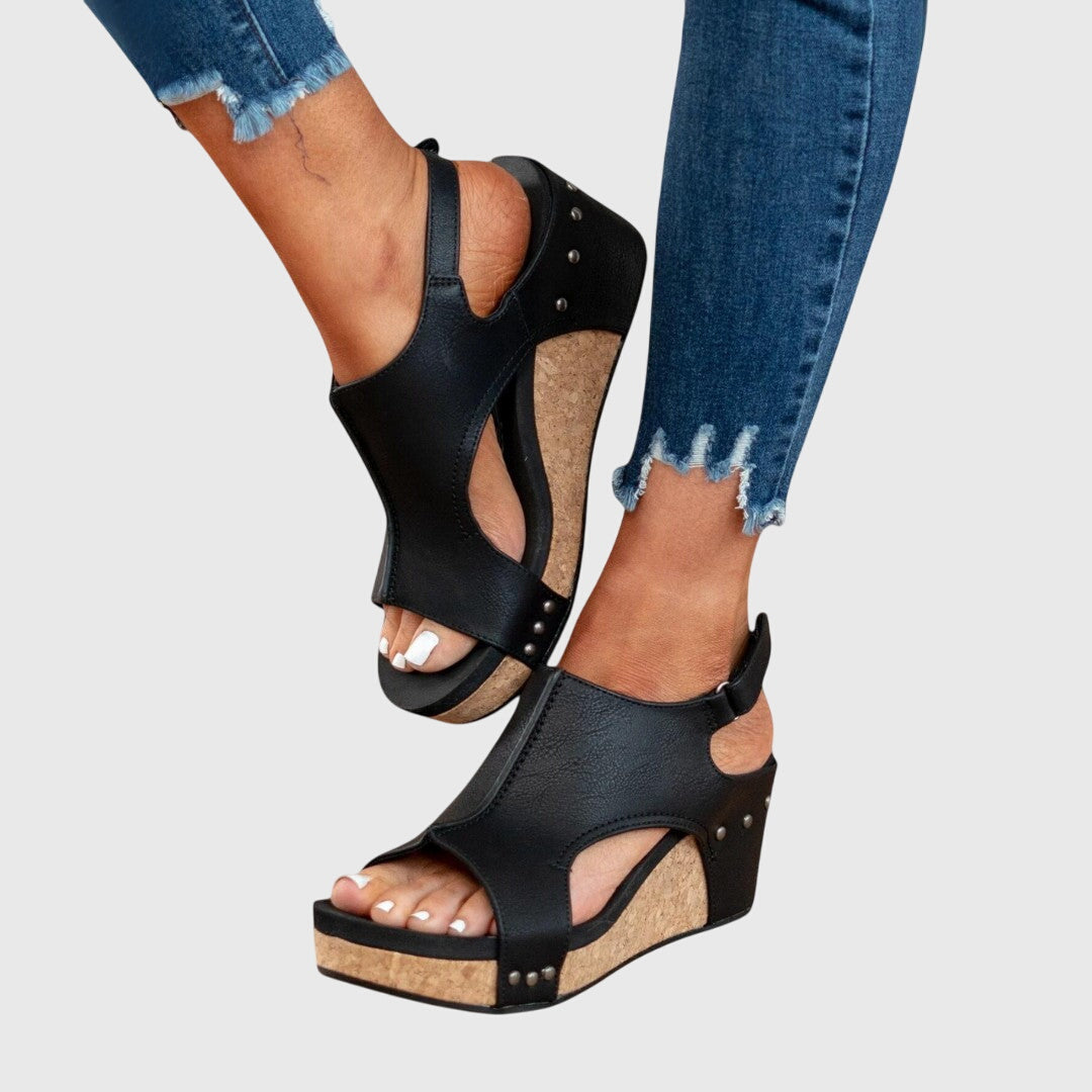 Black wedge sandals worn with blue jeans on a light gray background