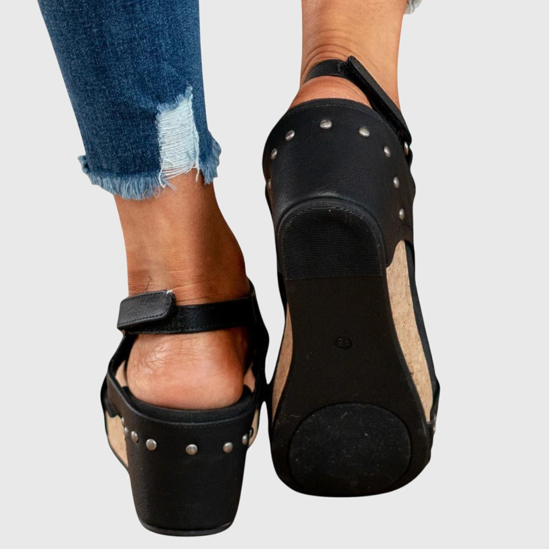 Black clog shoes with studded details worn with ripped jeans on a light gray background