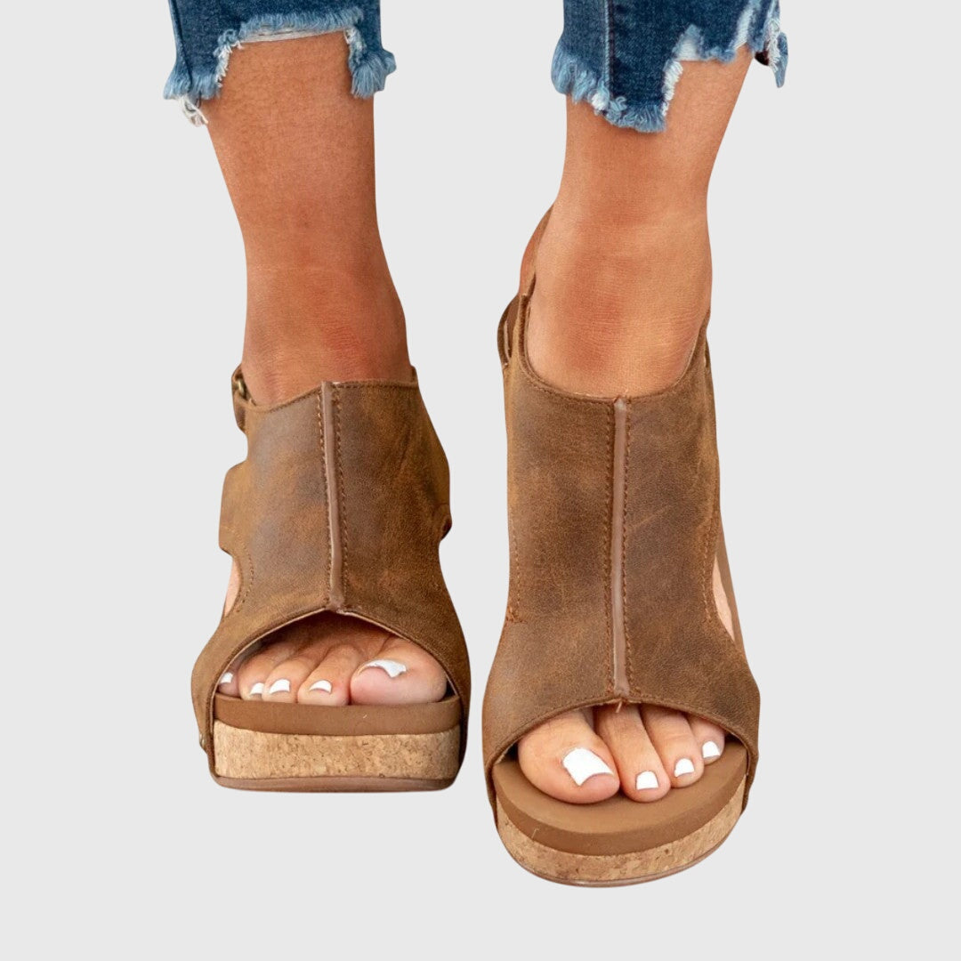 Brown open-toe wedge sandals worn with denim shorts on a light gray background