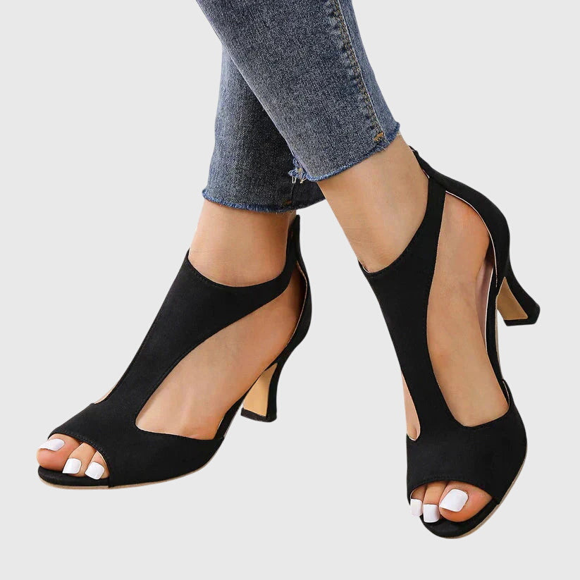 Black open-toe high-heeled shoes worn with blue jeans on a light gray background