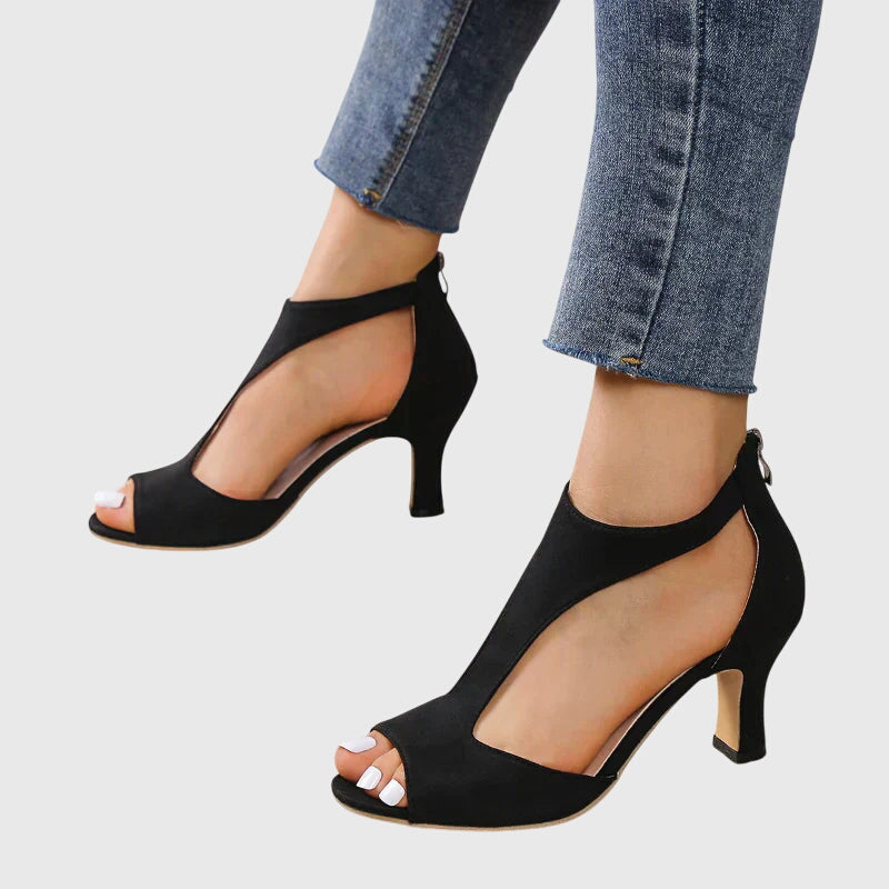 Black open-toe high-heeled shoes worn with blue jeans on a light gray background
