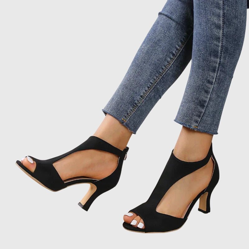 Black open-toe high-heeled shoes worn with blue jeans on a light gray background
