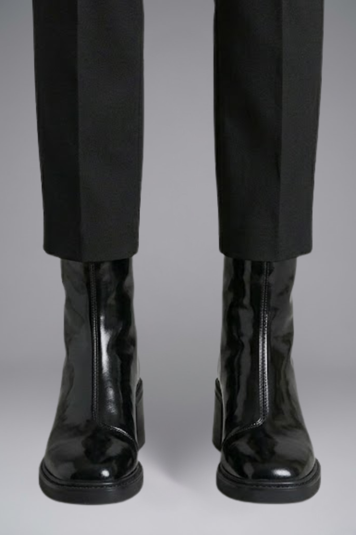 Black shiny boots worn with black pants on a gray background