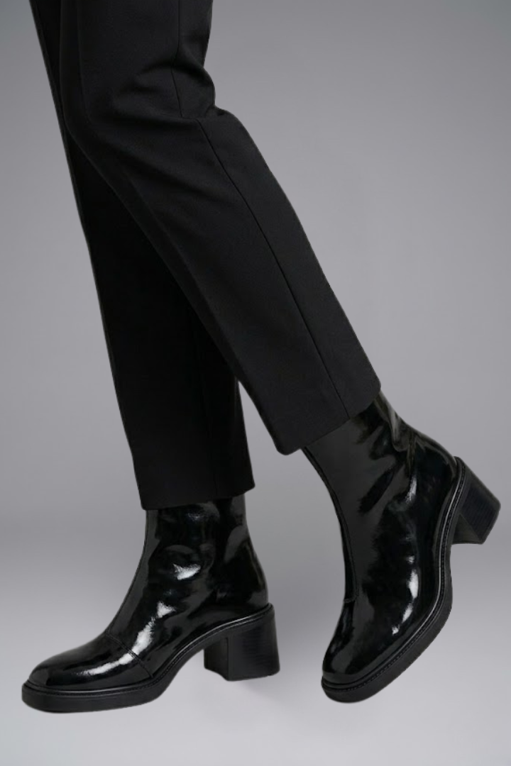 Black patent leather boots worn with black pants on a gray background