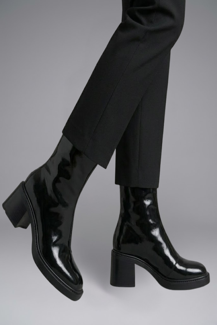Black patent leather boots worn with black pants on a gray background